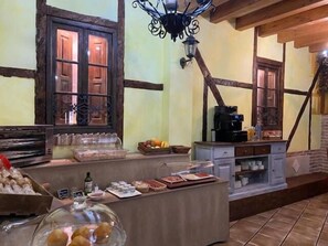 Una barra de desayuno con una máquina de café, fruta y bollería.
