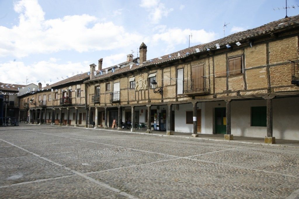 A cobblestone street with traditional buildings, balconies, and a clear sky.