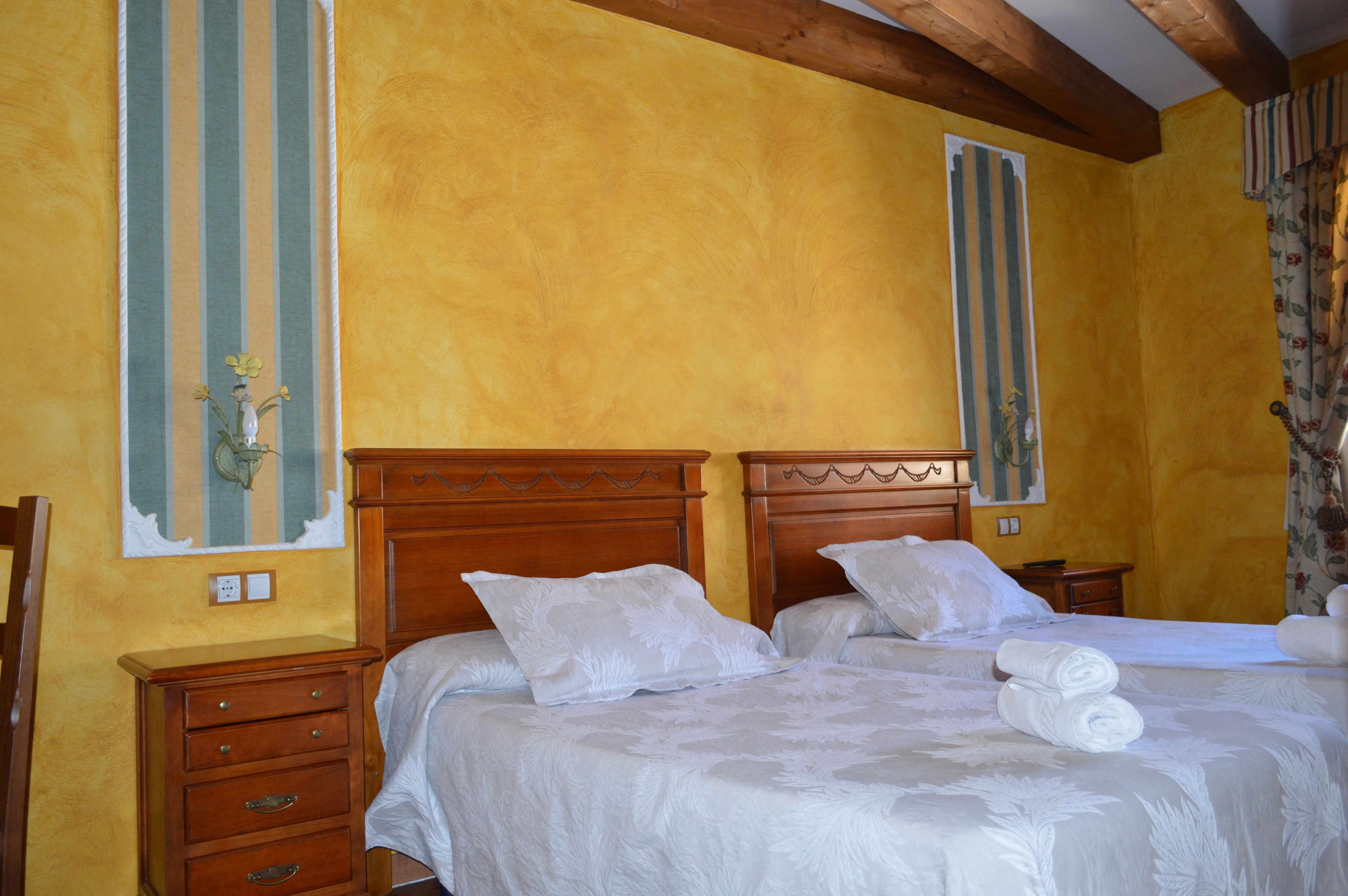 A hotel room with two wooden beds, white linens, and a wooden nightstand with a lamp.