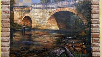 Una pintura de un puente de piedra sobre un río, con peces y una figura de pie en el puente.