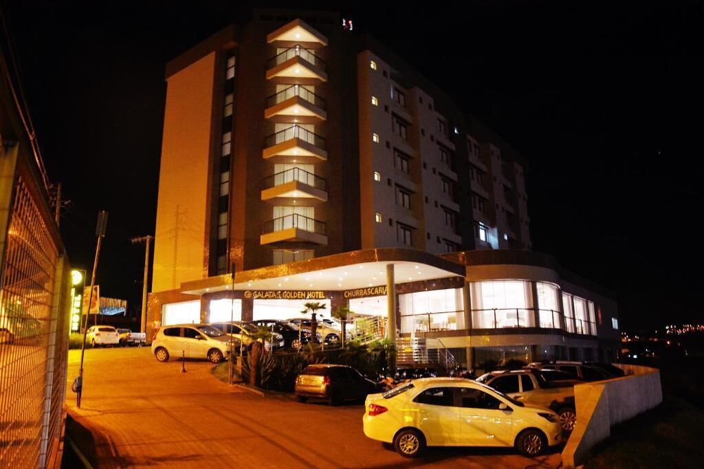 A hotel with a prominent entrance, multiple floors, and a parking area with cars.