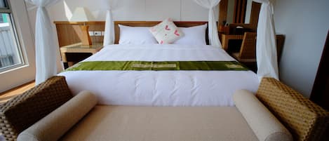A neatly made bed with white linens and a green accent, flanked by wicker chairs.