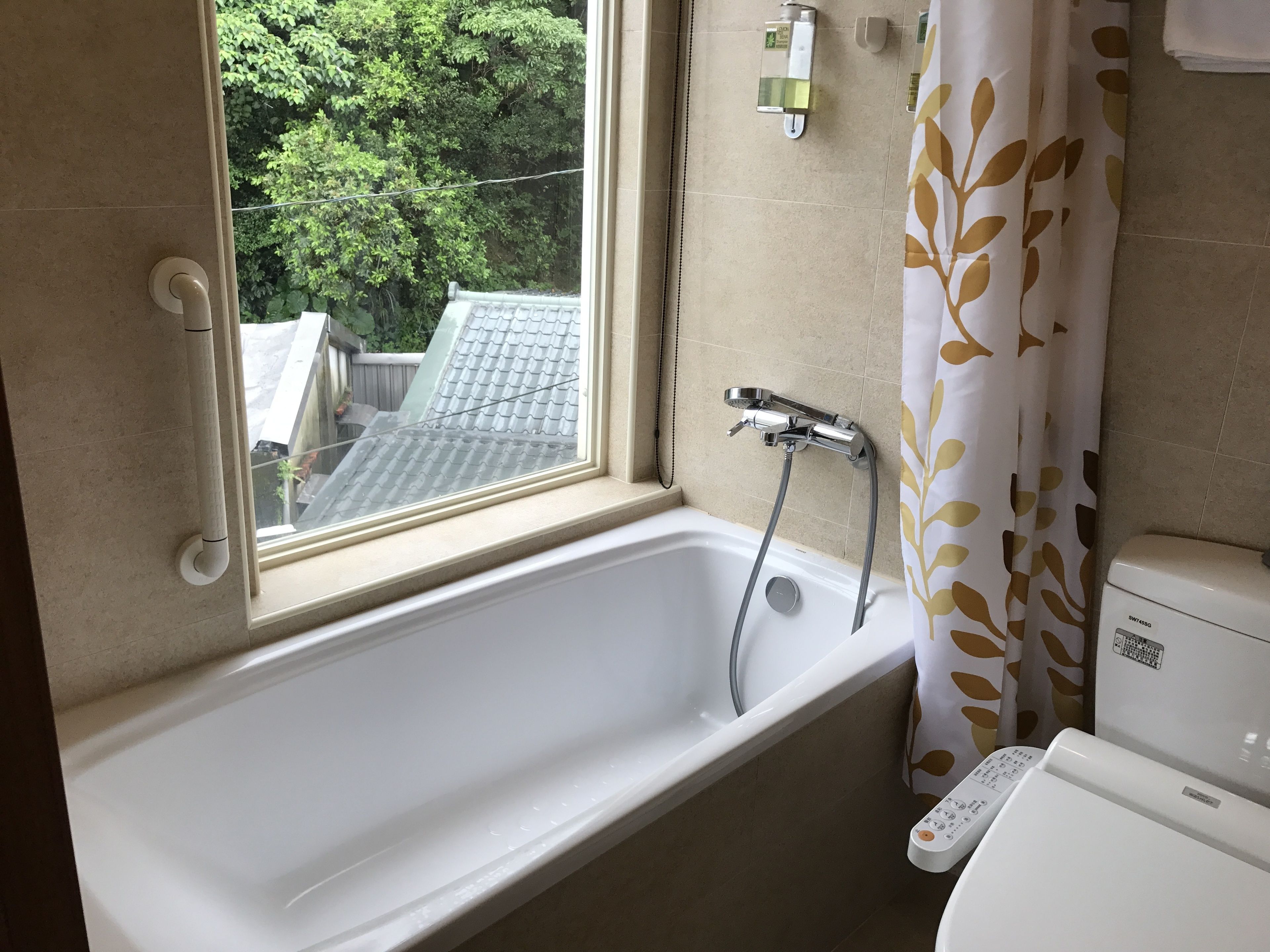 A bathroom with a bathtub, a window, a showerhead, and a toilet.