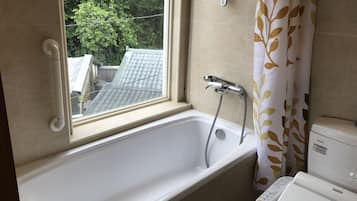 A bathroom with a bathtub, a window, a showerhead, and a toilet.