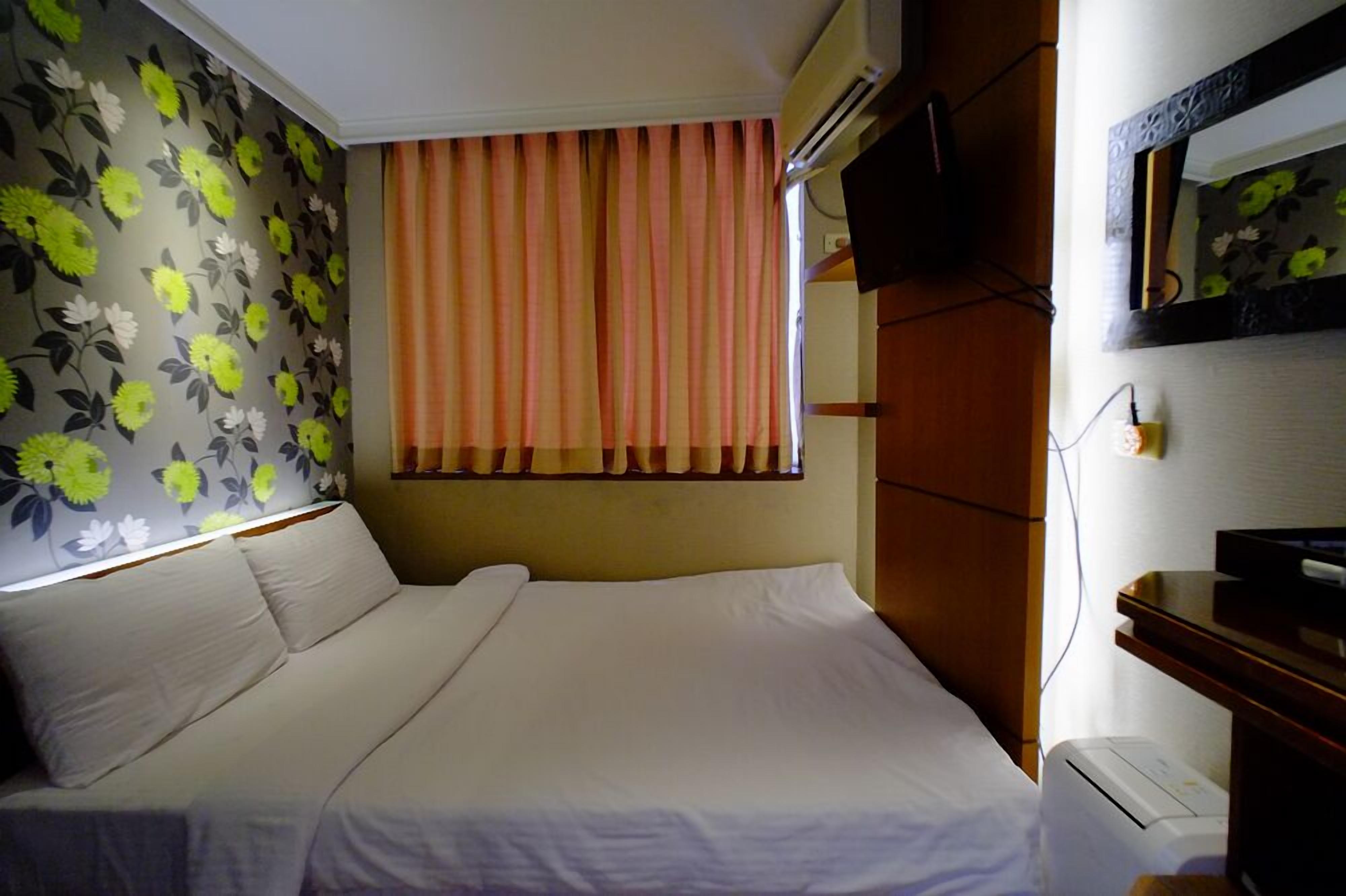 Una habitación de hotel con una cama, un televisor en la pared y una ventana con cortinas.