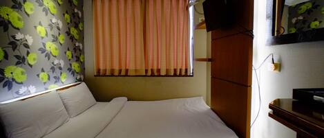 Una habitación de hotel con una cama, un televisor en la pared y una ventana con cortinas.