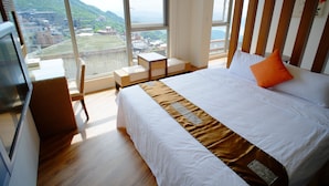 Une chambre d’hôtel avec un grand lit, une petite table et une chaise. Les fenêtres offrent une vue sur la ville et les montagnes.