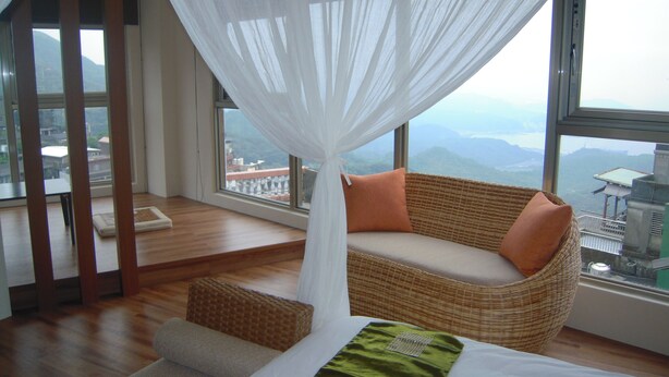 Une chambre avec une grande fenêtre, un canapé en osier, un lit et une vue sur les montagnes.