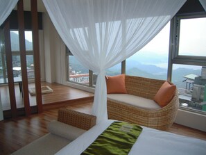 A bedroom with a large window, a wicker sofa, a bed, and a view of mountains.