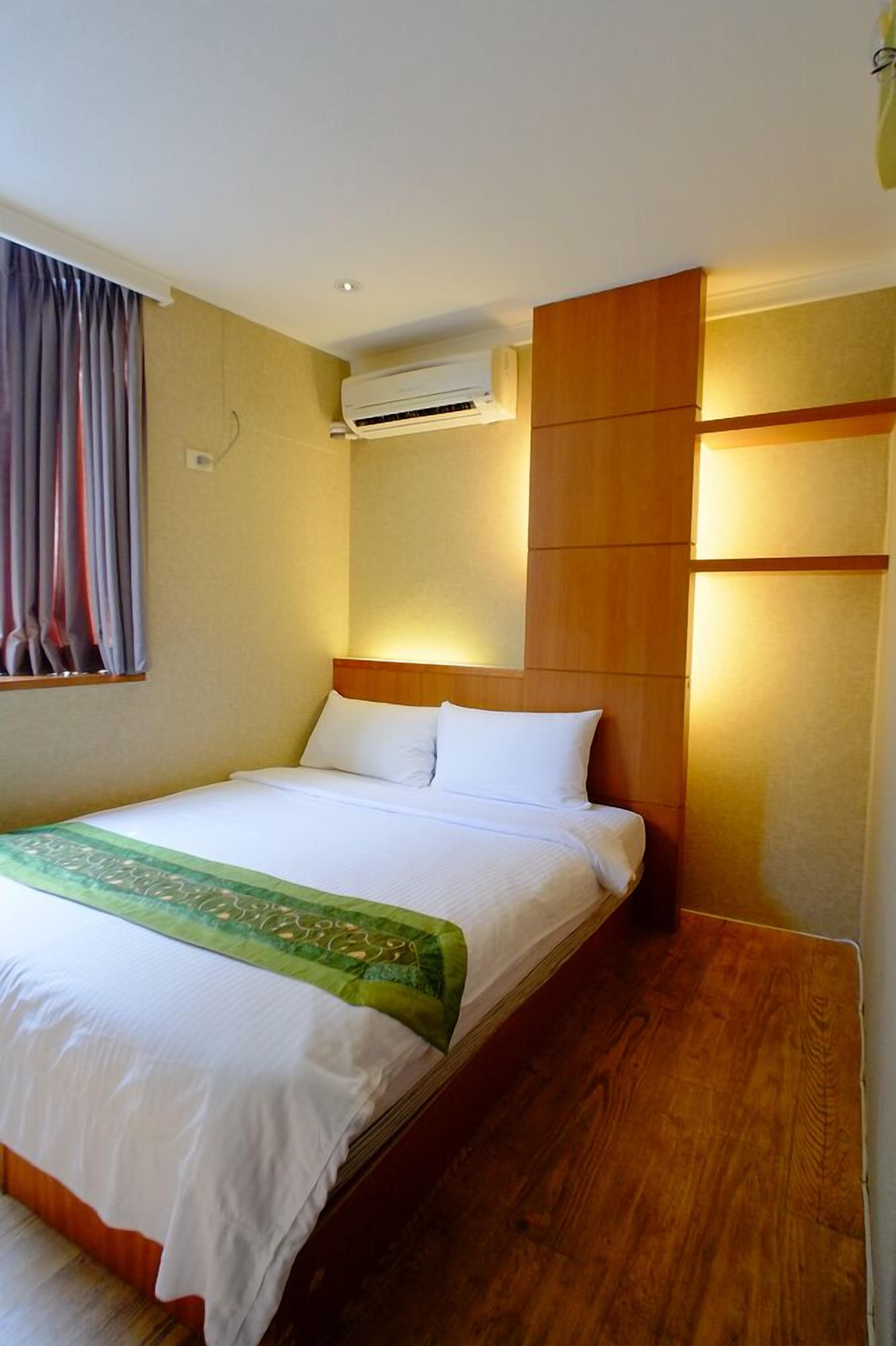 A hotel room with a bed, an air conditioning unit, wooden paneling, and a window with curtains.