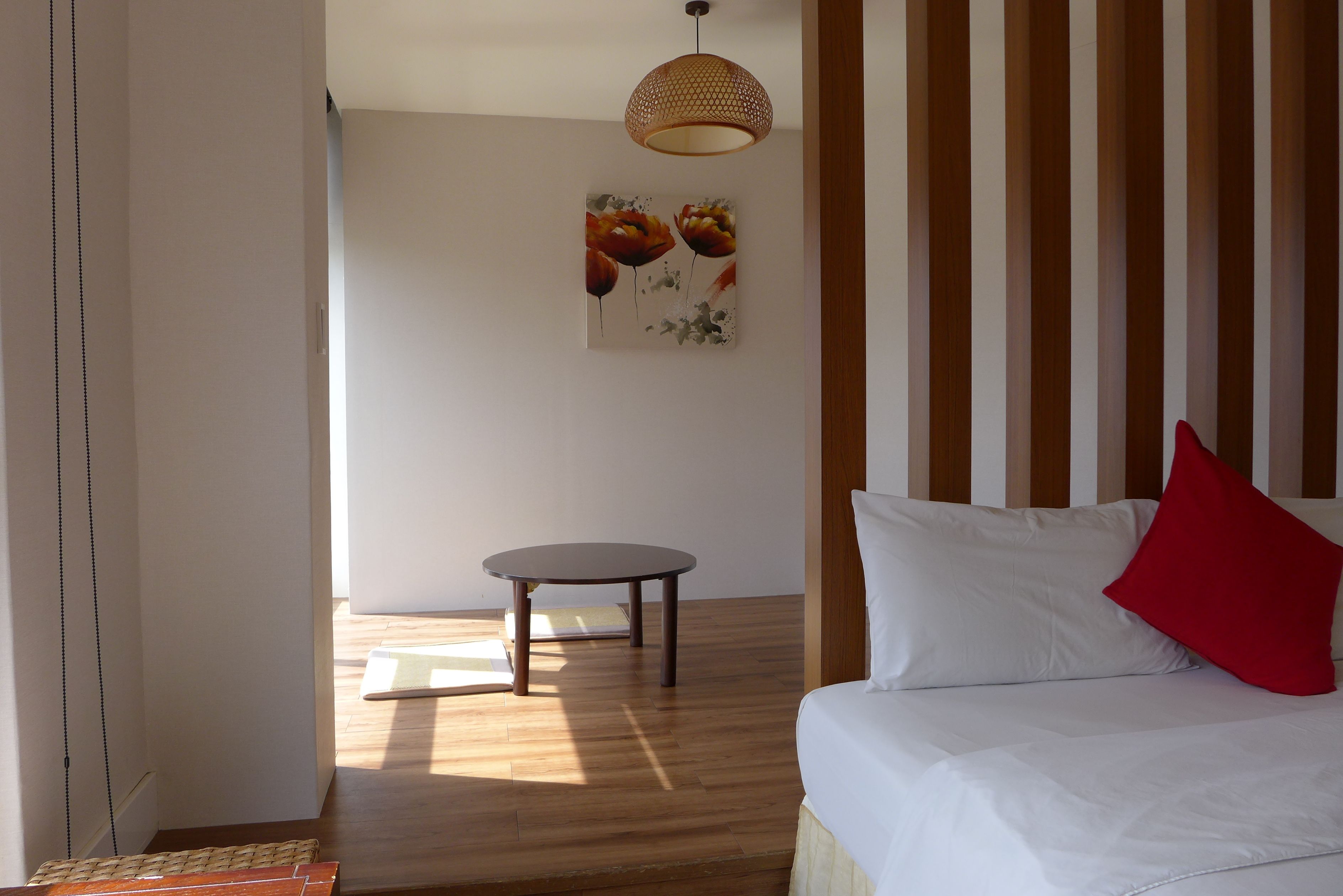 A bedroom with a bed, a small round table, and a hanging light fixture.
