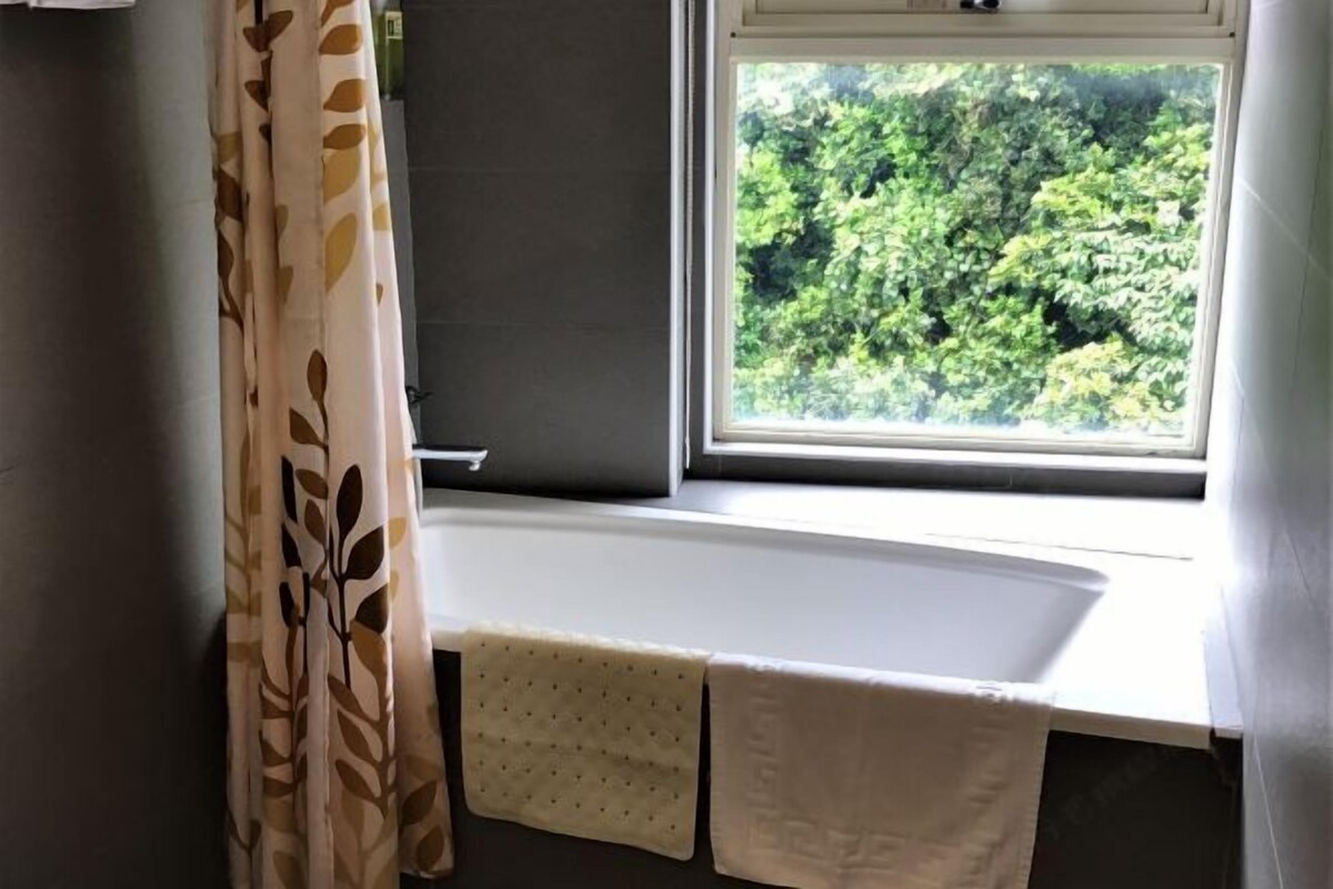Een badkamer met een raam, een bad en een handdoekrek met handdoeken.