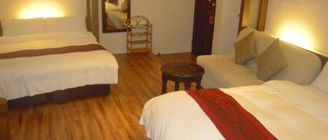 A hotel room with two single beds, a sofa, a small round table, and a mirror on the wall.