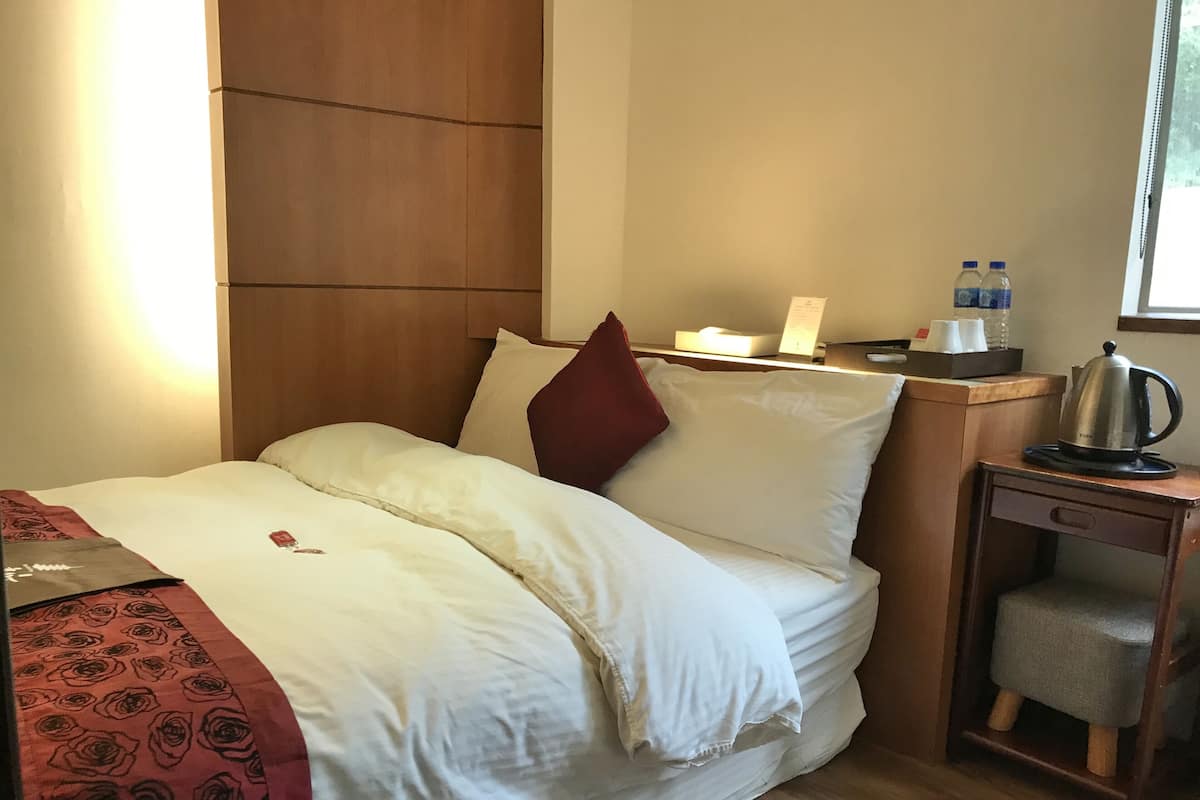 Ein Hotelzimmer mit einem Bett, einem Nachttisch, einem Wasserkocher und einem Fenster.