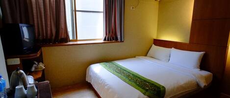Habitación de hotel con cama, escritorio con televisor, ventana con cortinas y equipo de aire acondicionado.