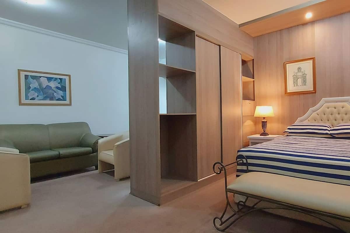A hotel room with a bed, a green sofa, a small table, and a wall with framed pictures.