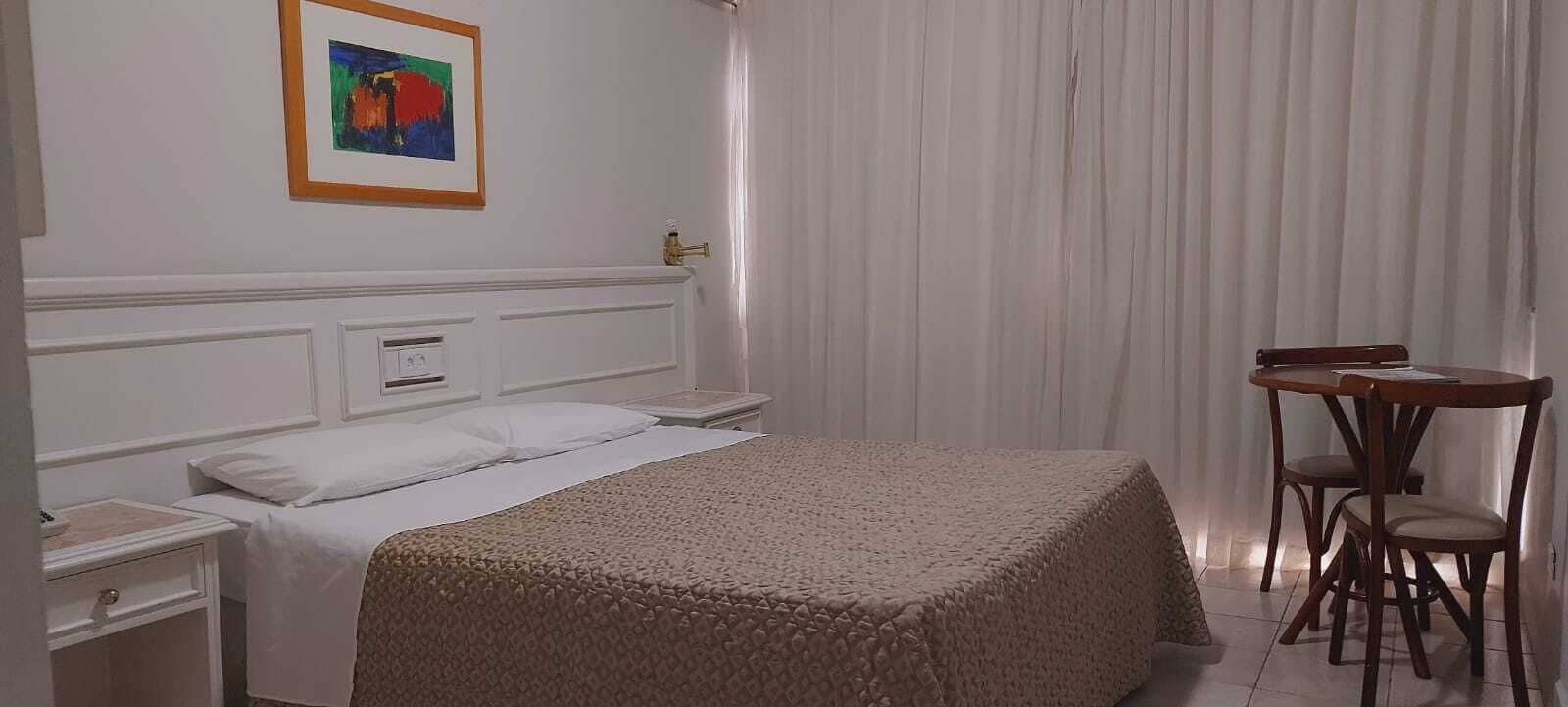 Quarto de hotel com uma cama, mesa de cabeceira, cadeira e uma mesa com cadeira.