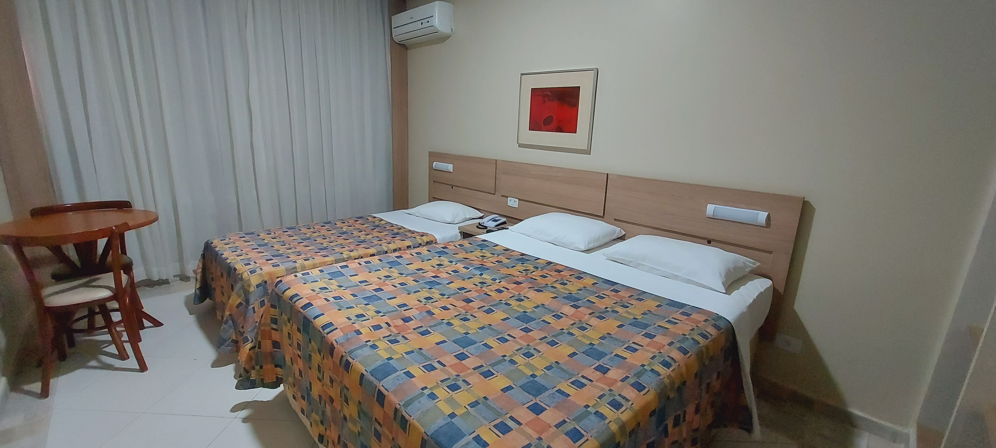 A hotel room with two beds, a wooden headboard, a small table, and a chair.