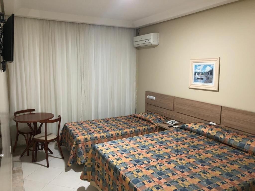 Habitación de hotel con dos camas, un escritorio, una silla, un equipo de aire acondicionado y un cuadro en la pared.