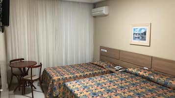 Habitación de hotel con dos camas, un escritorio, una silla, un equipo de aire acondicionado y un cuadro en la pared.