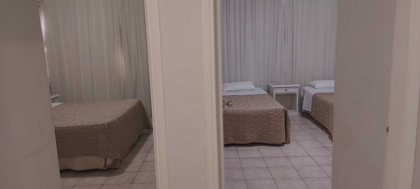 A hotel room with two beds, a small bedside table, and a curtain.