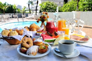 A breakfast buffet with pastries, fruits, and beverages by a poolside. - Jandaia Hotel Campo Grande (Campo Grande)