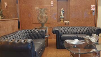 Um hall com dois sofás de couro preto, uma mesa de centro de vidro, um vaso decorativo e uma estátua na parede.