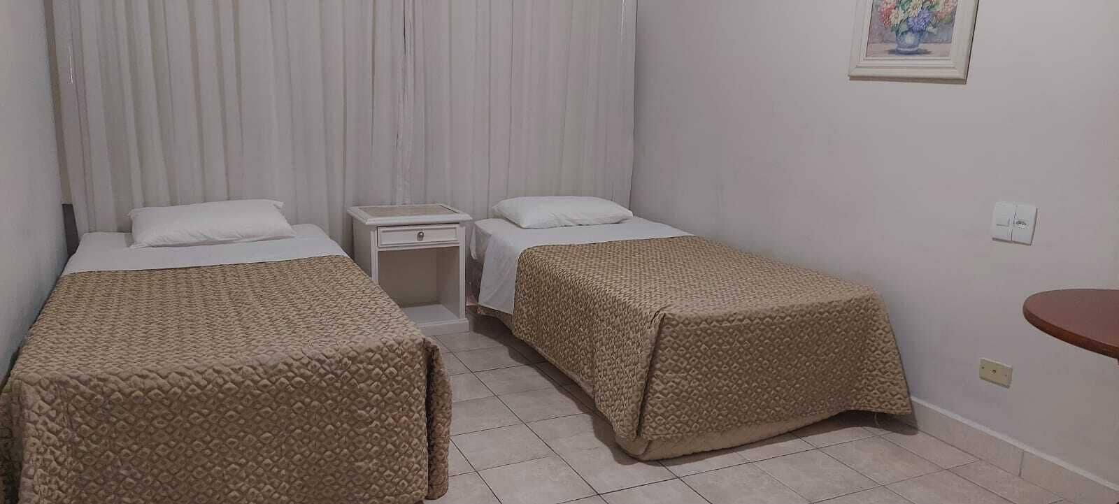 A room with two beds, each with a patterned bedspread, a bedside table, and a nightstand.