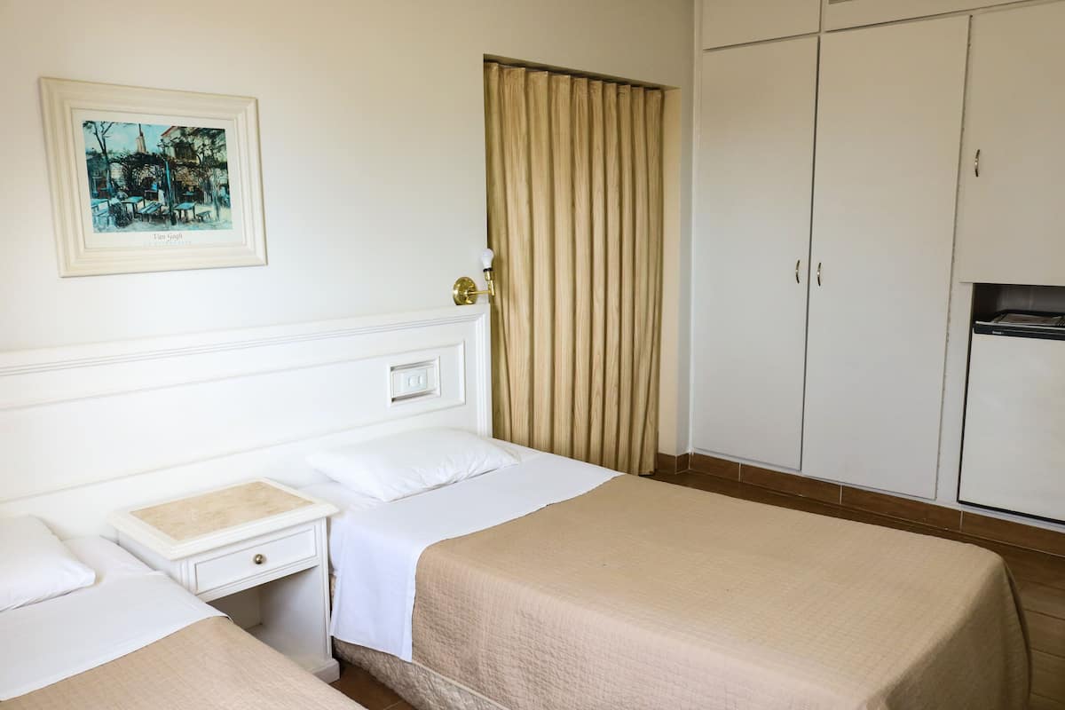 A hotel room with two beds, a nightstand, a framed picture on the wall, a wardrobe, and a curtain.