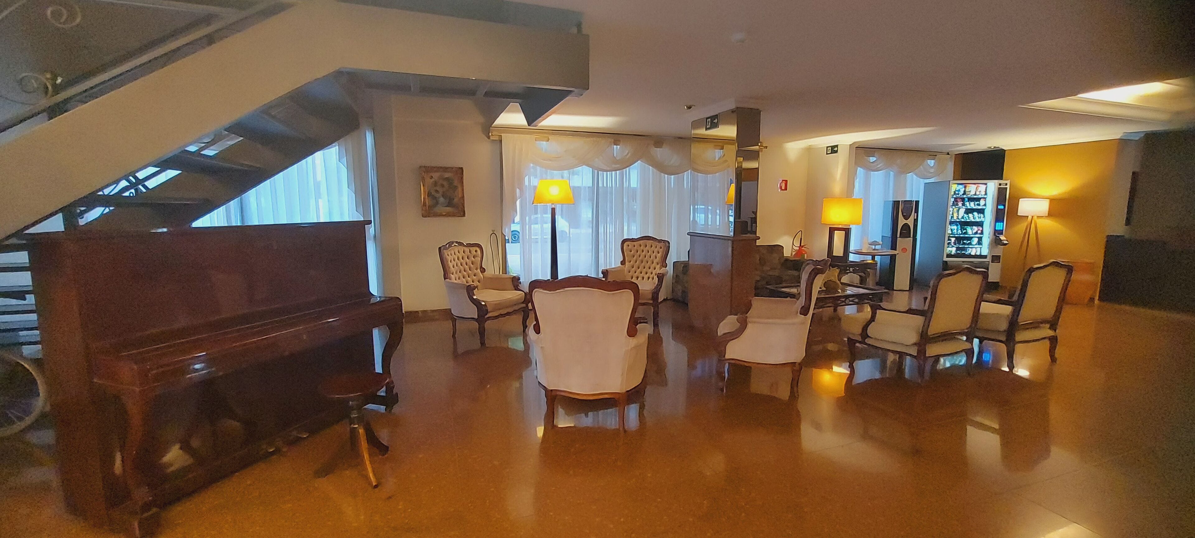 Eine geräumige Lobby mit einem Flügel, bequemen Sitzgelegenheiten, einem Verkaufsautomaten und einer Treppe.
