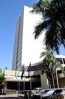 Um hotel alto com fachada curva, várias bandeiras e um estacionamento com carros.