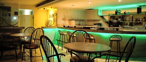 A restaurant with a bar area, multiple tables and chairs, and a kitchen in the background.