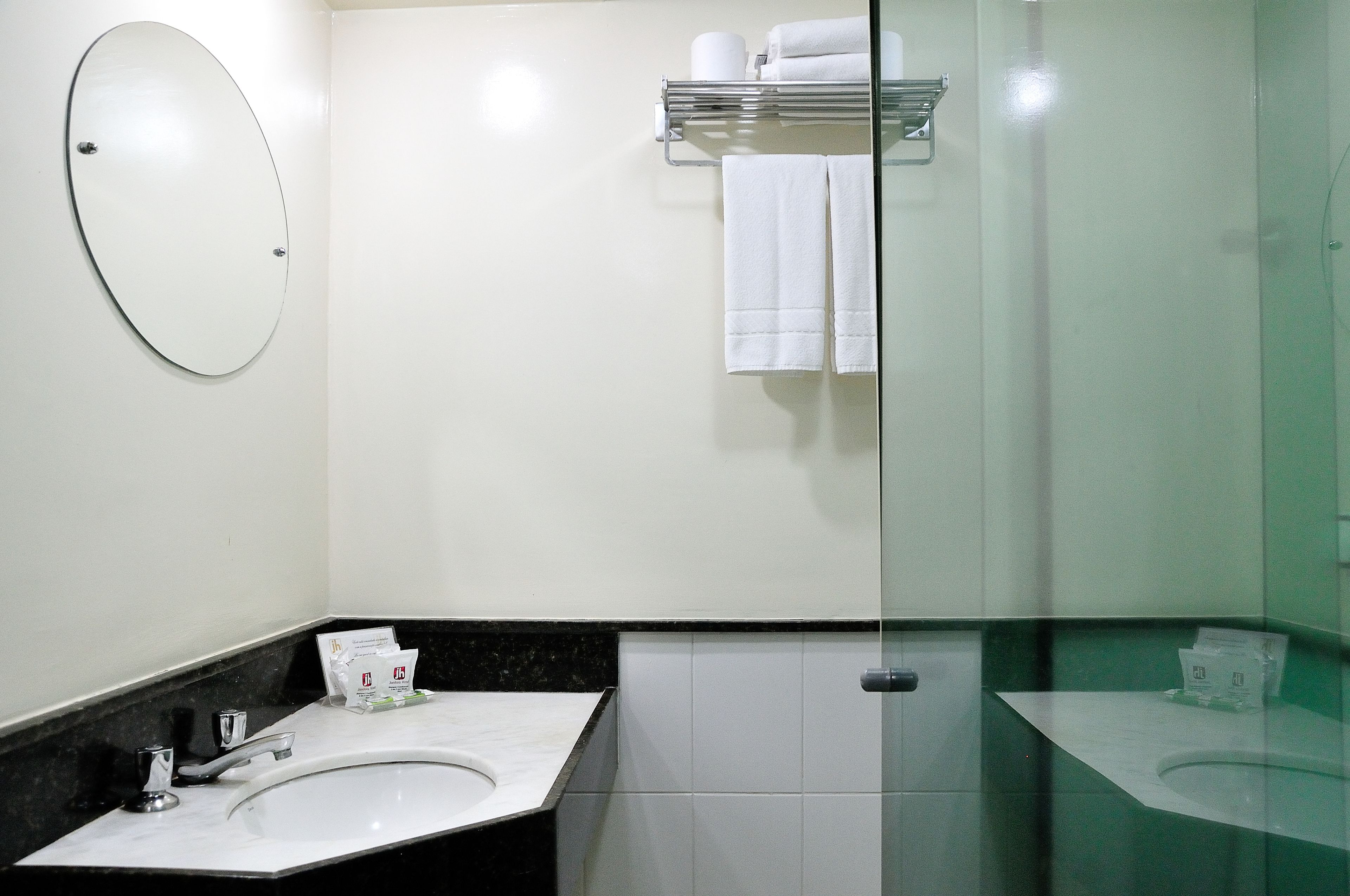 A bathroom with a round mirror, two sinks, a glass shower enclosure, and a towel rack with folded towels.