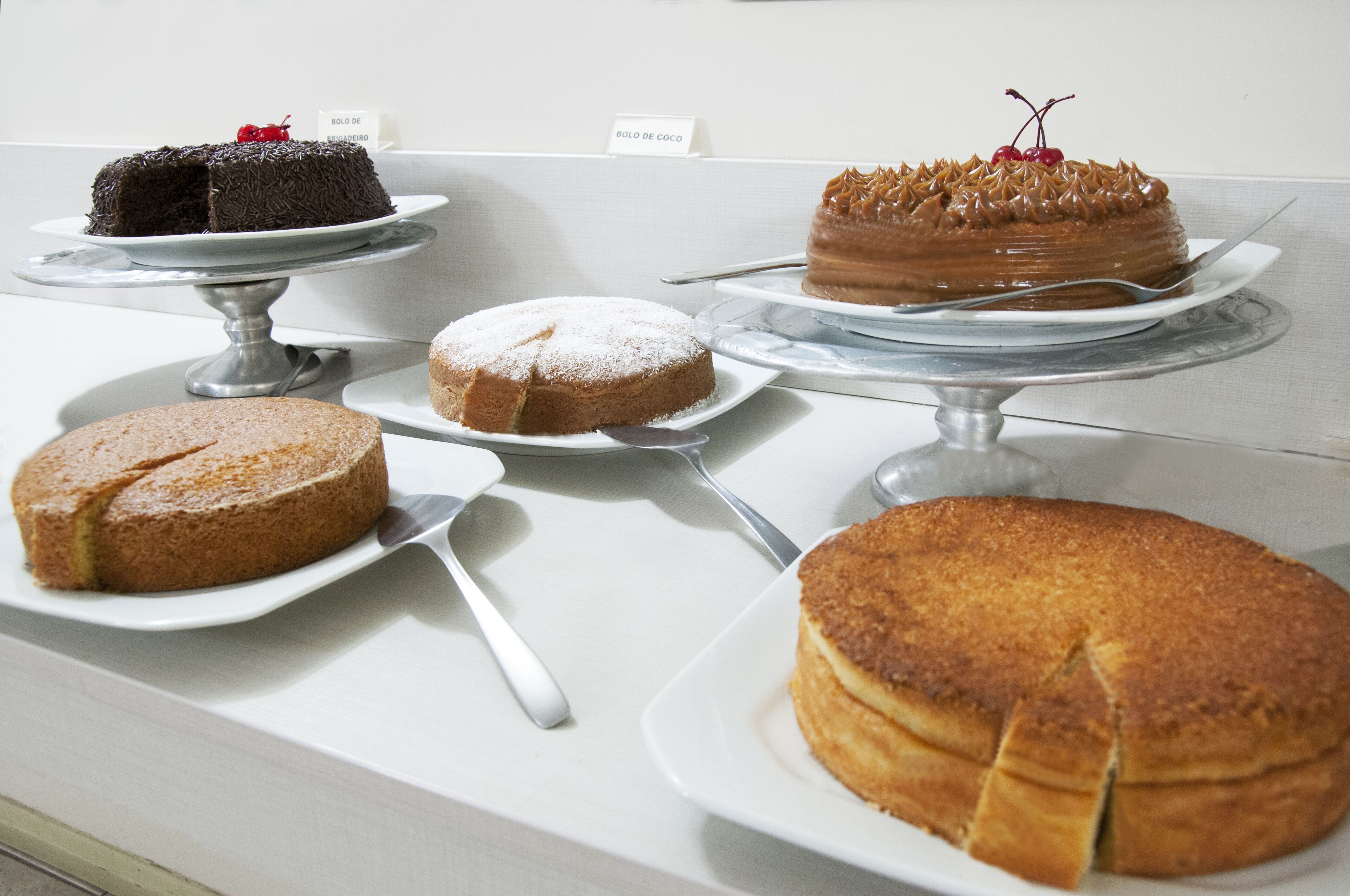 A display of various cakes on white plates with cake servers.