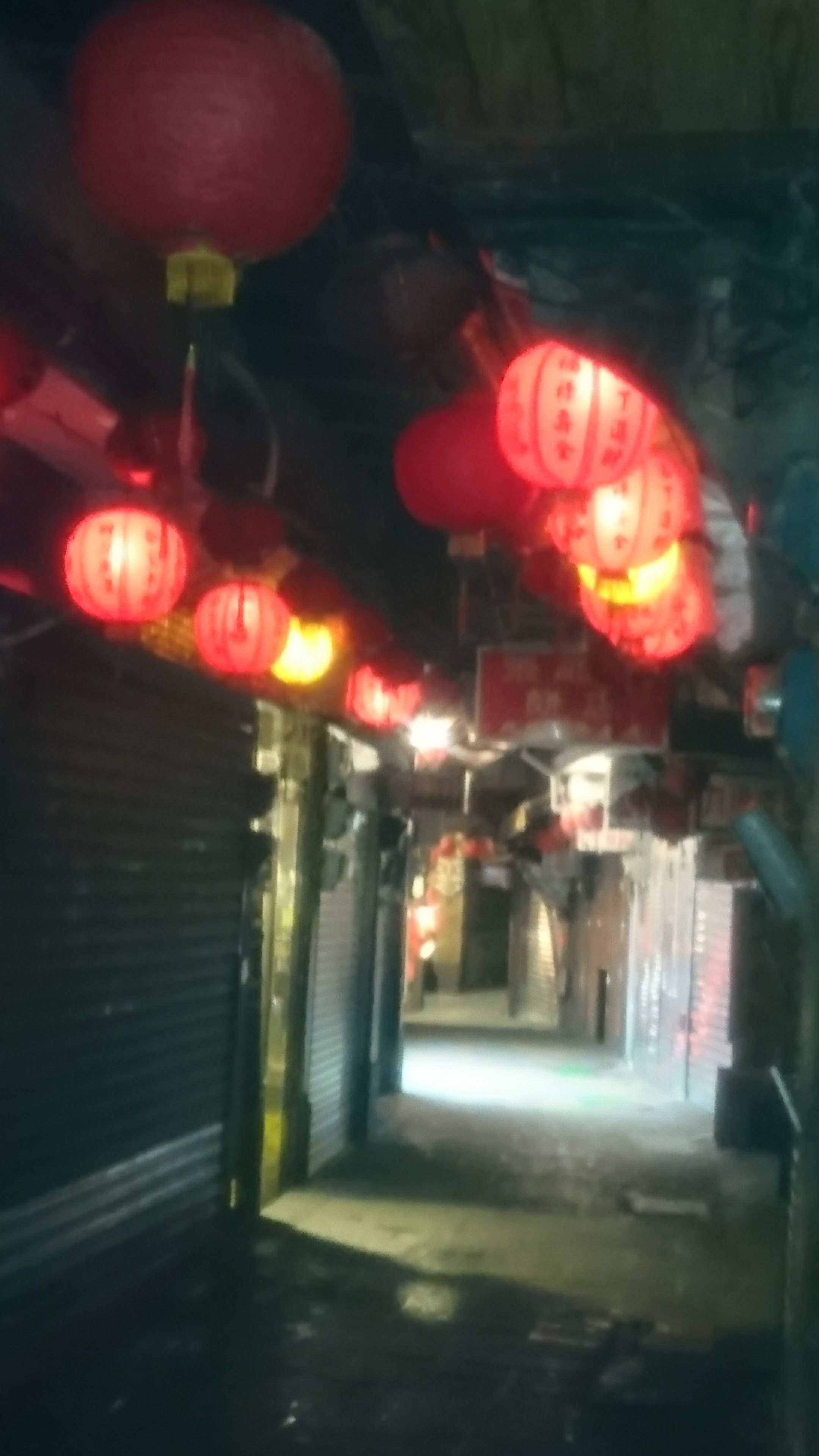 A corridor with red lanterns hanging from the ceiling, leading to closed shops.