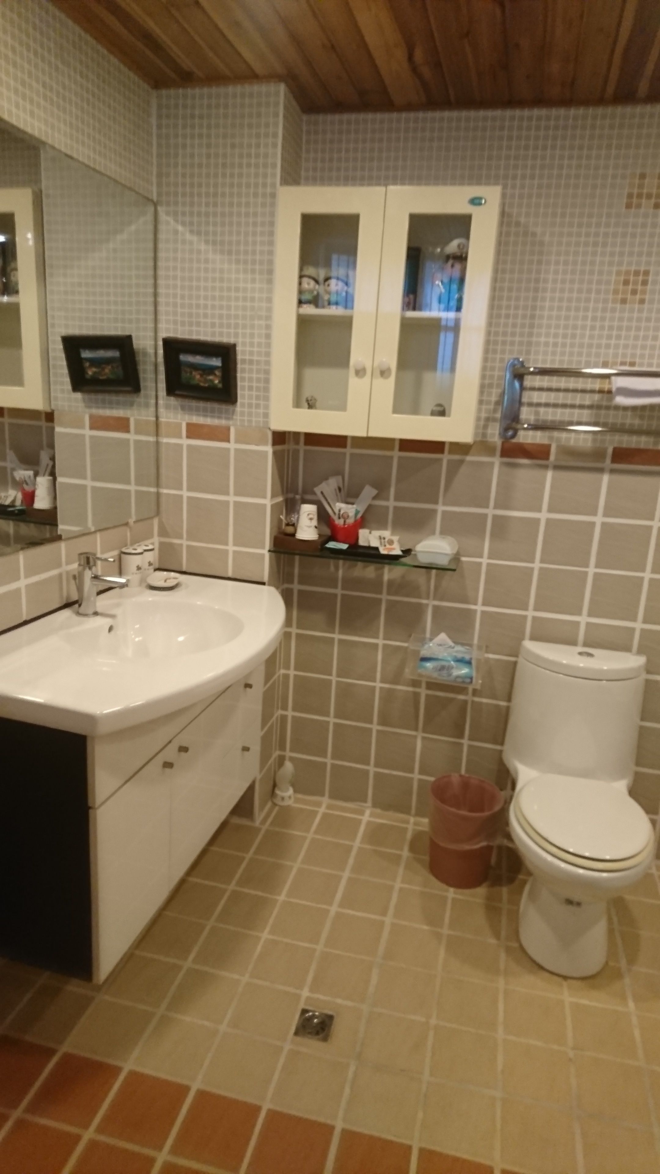 A bathroom with a white sink, mirror, cabinets, and a toilet.