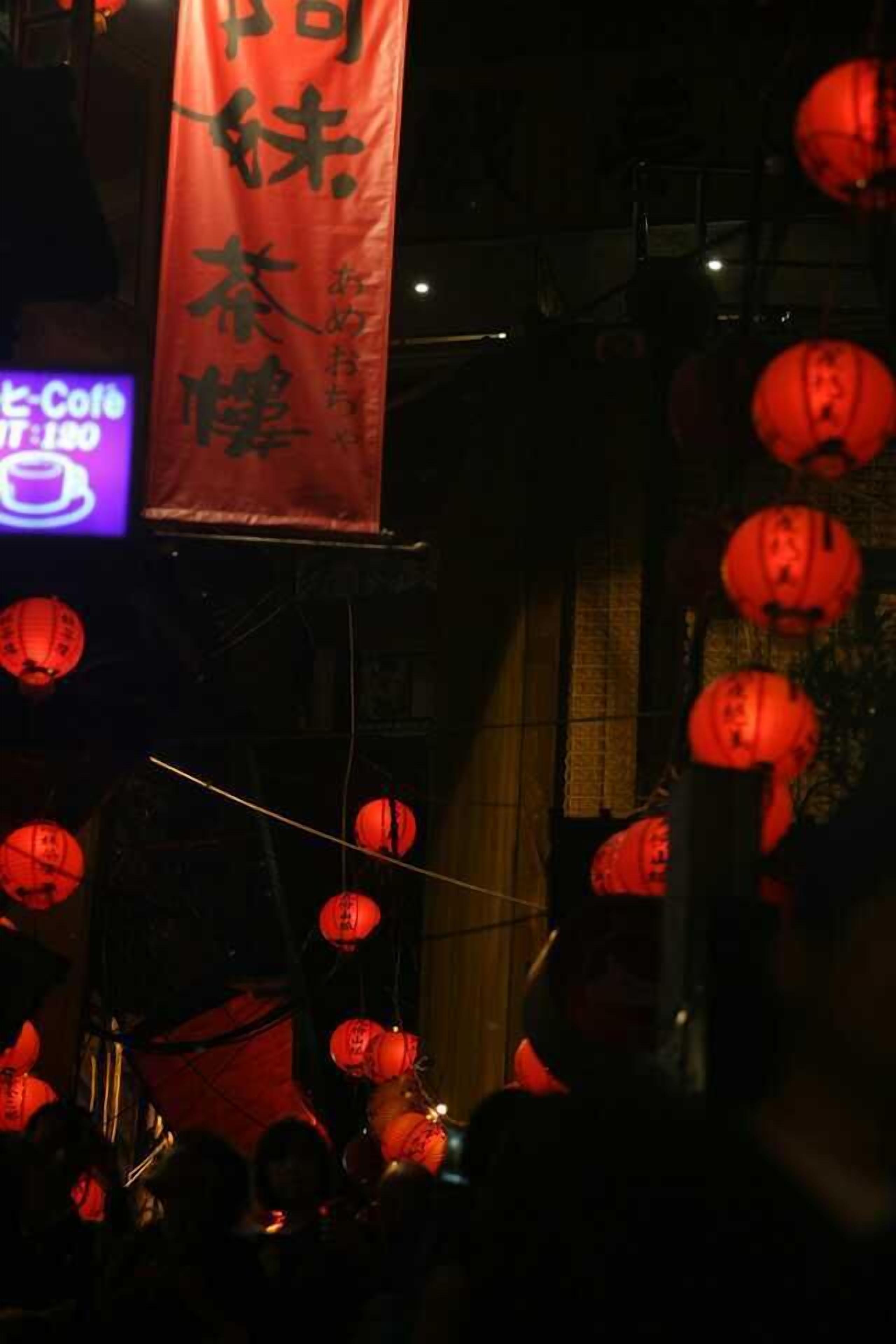 Un espacio interior tenuemente iluminado con gente, faroles rojos y un estandarte con caracteres chinos.