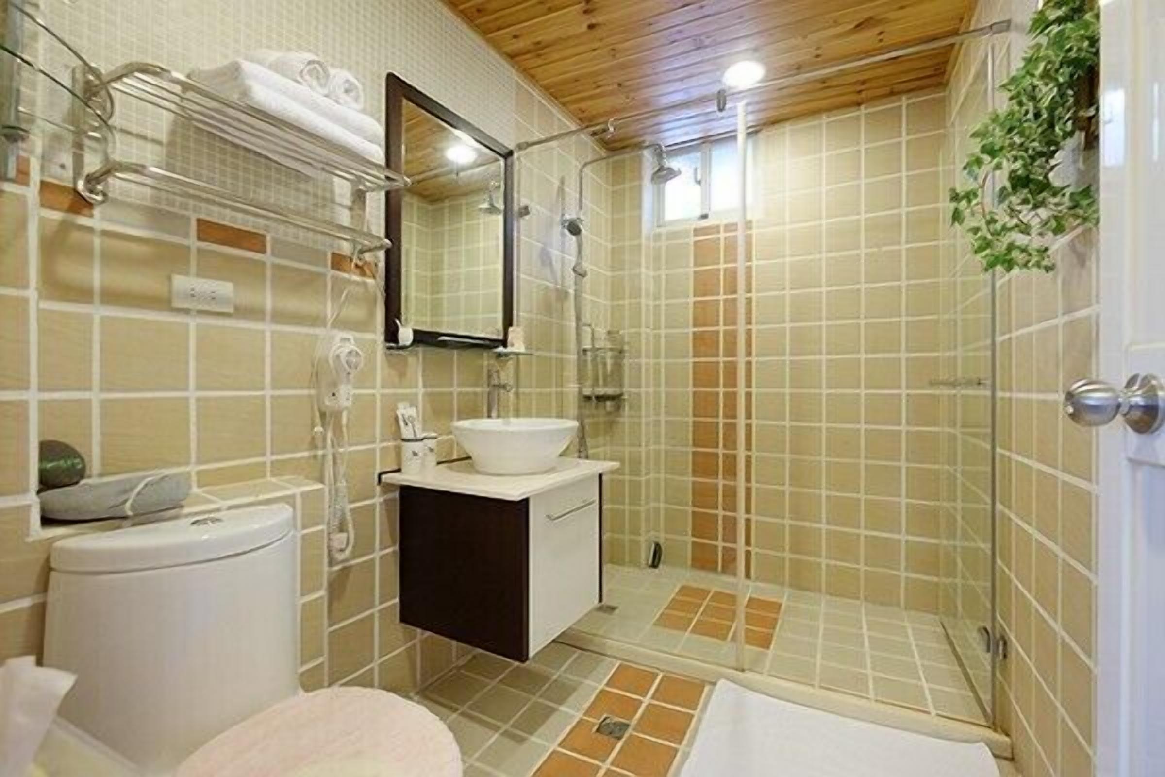 A bathroom with a toilet, sink, mirror, shower, and tiled walls.