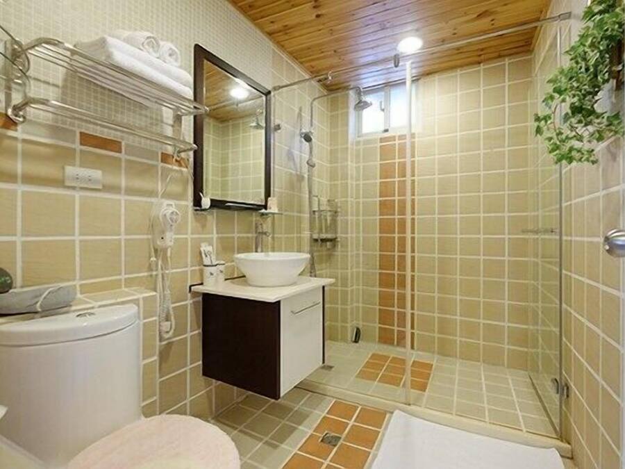A bathroom with a toilet, sink, mirror, shower, and tiled walls.