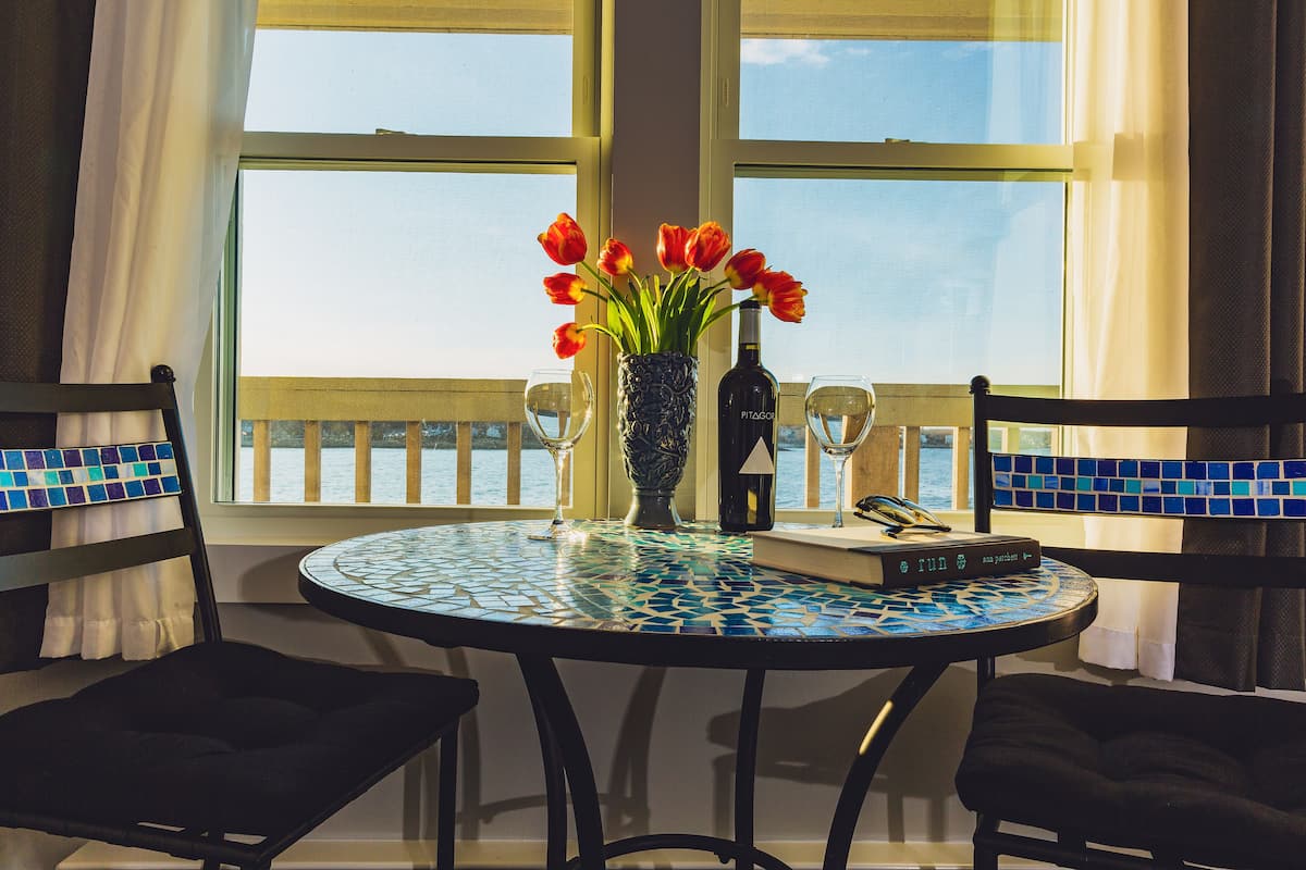 Une table ronde avec un plateau en mosaïque, deux chaises, un vase avec des fleurs rouges, une bouteille et un livre intitulé « Run ».
