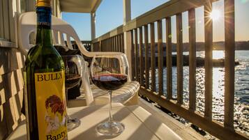 A bottle of BULLY wine and a glass on a table by a railing with a view of a body of water and the sun setting.
