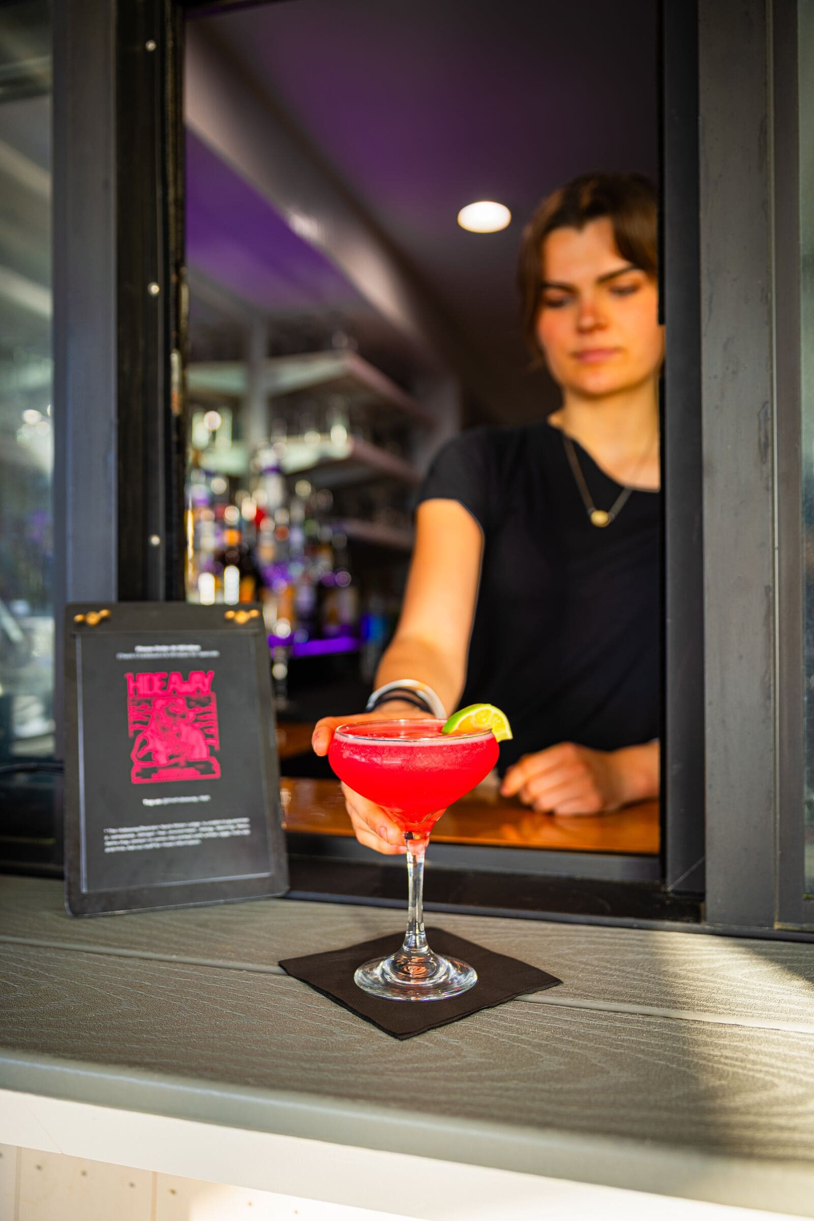 A bar area with a red cocktail on the counter, a menu, and a person behind the bar.