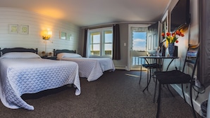 A hotel room with two beds, a small table with a chair, a TV, and a view of the sea through the window. - Bearskin Neck Motor Lodge (Rockport)