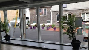 A view from inside a room with large windows overlooking a street. There are potted plants on the windowsill and outside. - Bearskin Neck Motor Lodge (Rockport)