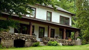 A two-story house with a stone foundation, a porch with wooden railings, and a small stone fireplace. - Rock Castle Resort (Lake George)