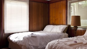A bedroom with two beds, wooden paneling on the walls, and a lamp on the nightstand. - Rock Castle Resort (Lake George)