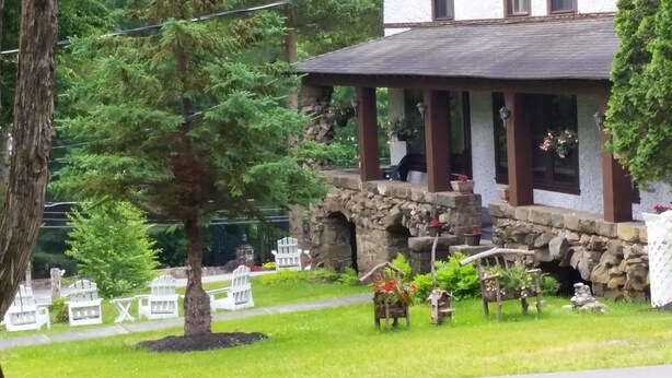 A stone building with a covered porch, surrounded by greenery and white chairs. - Rock Castle Resort (Lake George)