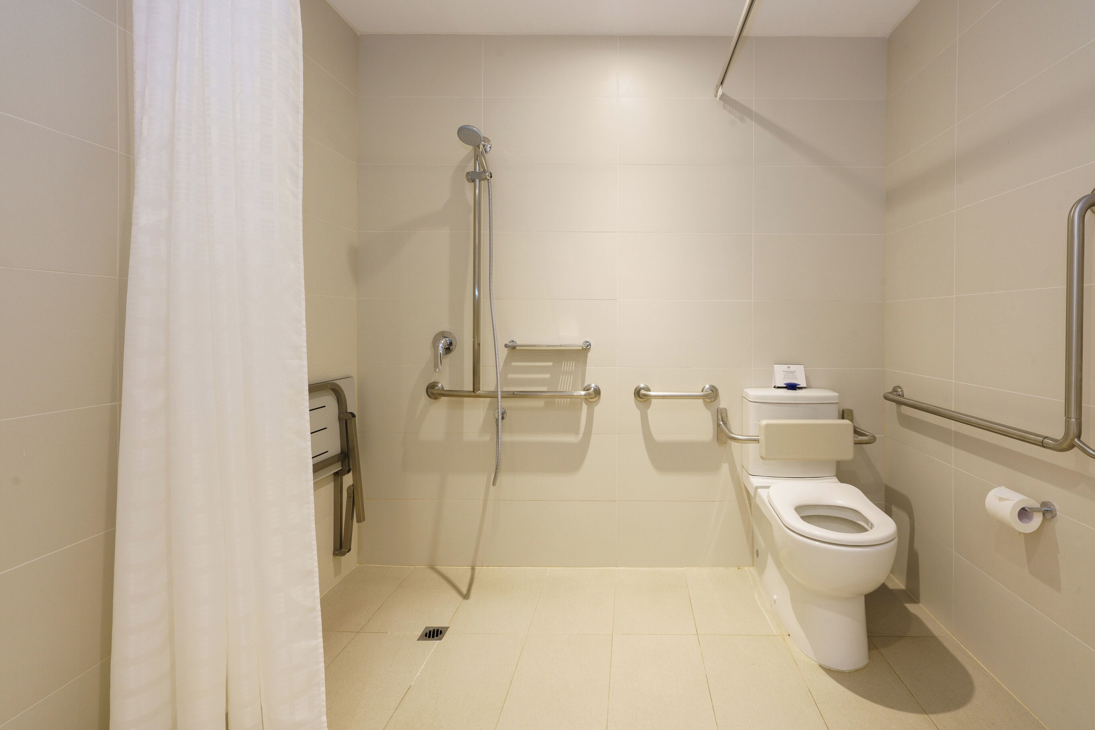 A bathroom with a shower, toilet, and handrails.