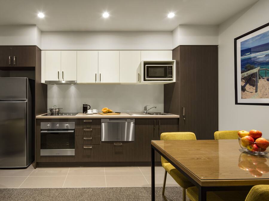 Una cocina moderna con electrodomésticos de acero inoxidable, microondas y comedor con mesa de madera y sillas amarillas.