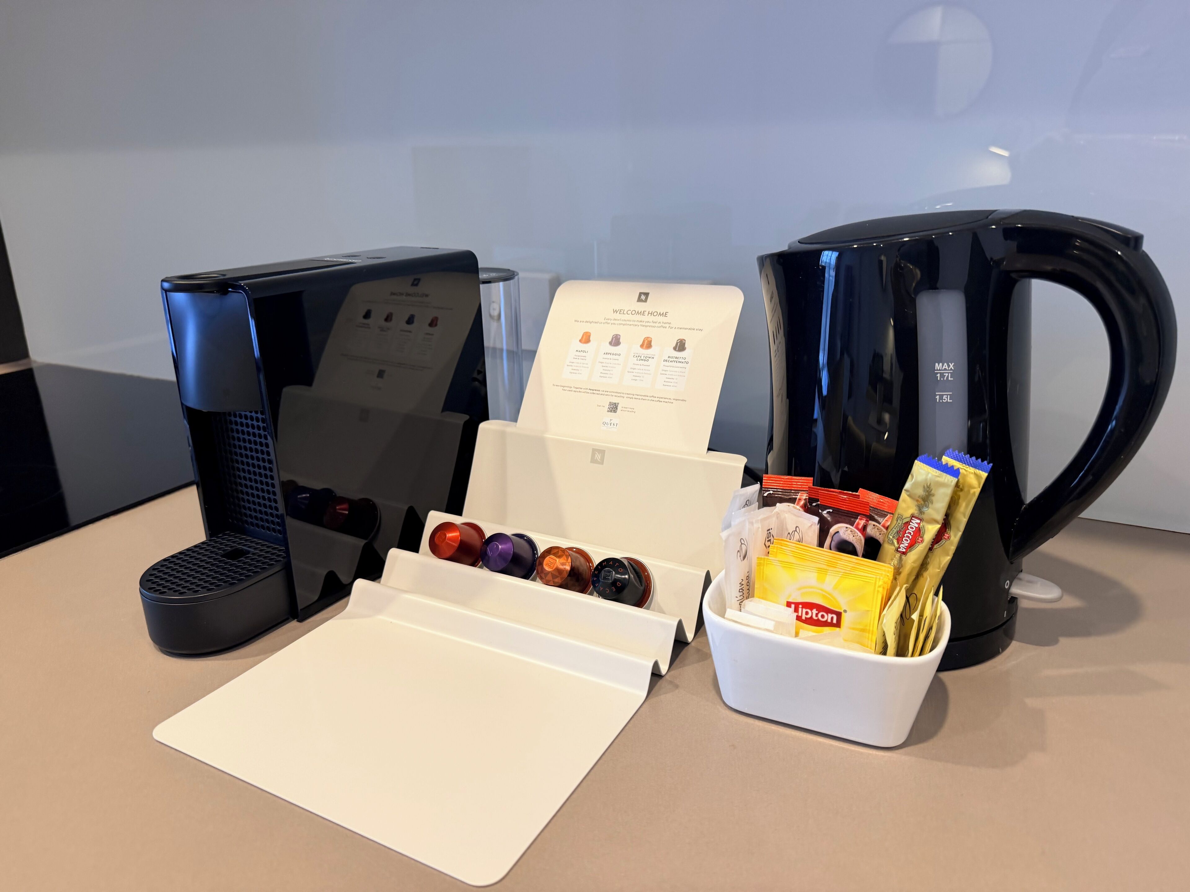 A coffee station with two coffee makers, a menu, and a cup holder with coffee pods and a Lipton tea bag.